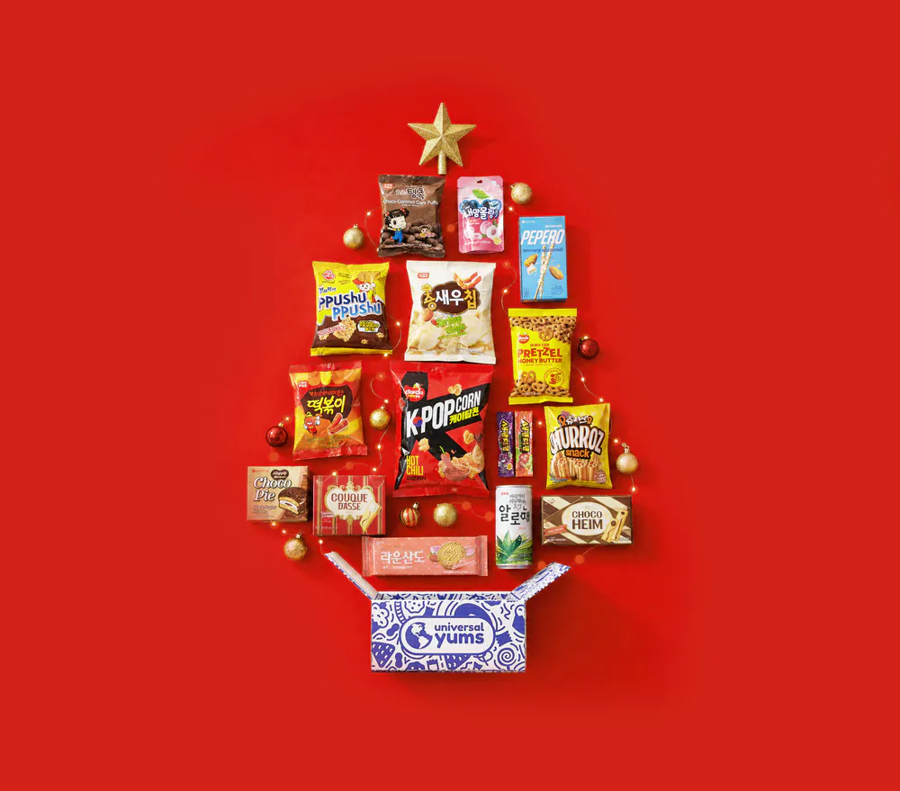 Korean snacks arranged in the shape of a holiday tree above an open Universal Yums box.